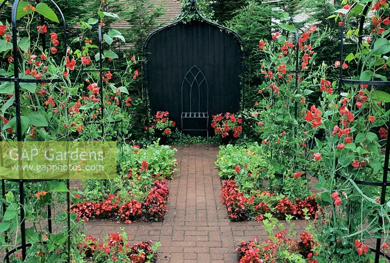 Überdachter Sitz im formellen Garten mit Lathyrus - Sweetpeas Bouquet-Serie (Scharlachrot) auf Obelisken im roten Garten mit Farbmotiv in Little Cottage, Hampshire