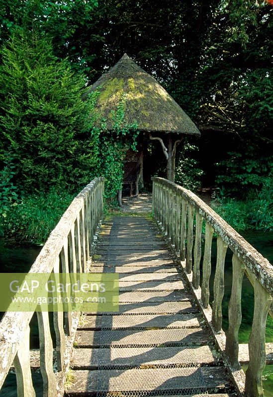 Holzbrücke über den Fluss, der zum rustikalen strohgedeckten Sommerhaus führt - Weir House, Hants