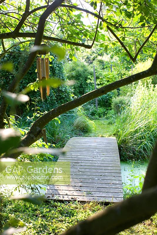 Weg, der über Holzbrücke, Teich im Garten mit Bambus- und Windspielen im Baum führt