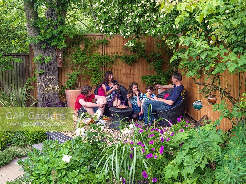 Die Familie Monaghan entspannt sich in einem schattigen Sitzbereich am Fuße ihres modernen Stadtgartens Muswell Hill in London.