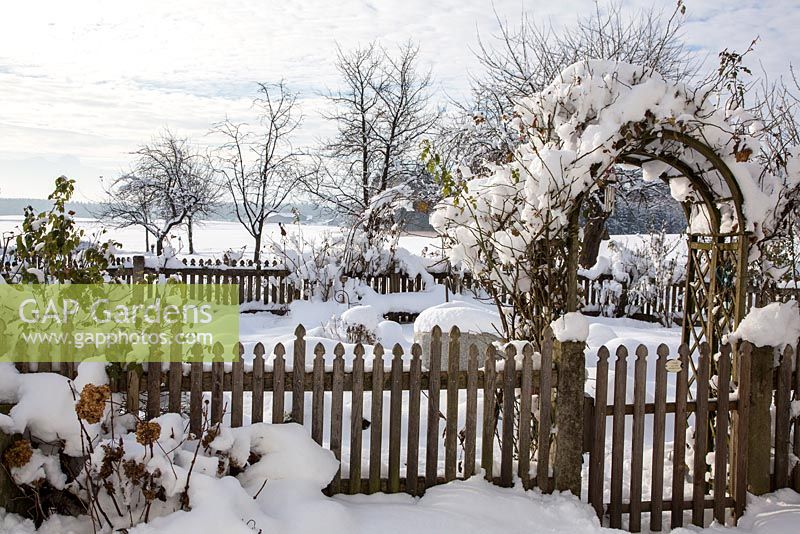 Winterszene mit Bauerngarten, umgeben von einem Holzzaun
