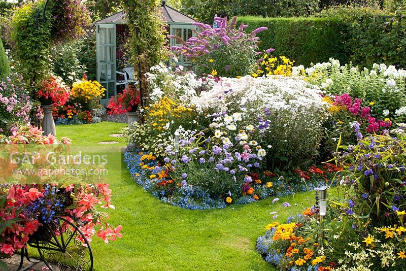 Bunter Garten mit gemischten Beeten, gefüllt mit zarten einjährigen Pflanzen, Sträuchern und Stauden. Sommerhaus und Rasen. Manvers Street, Derbyshire NGS August