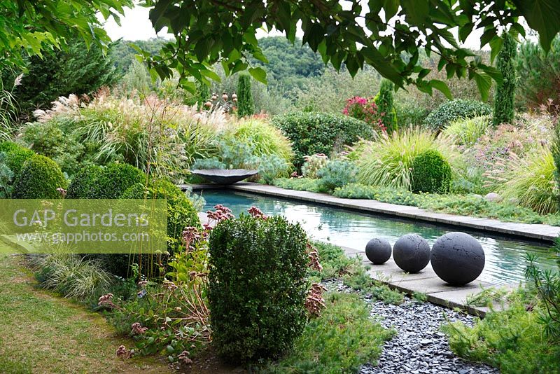 Drei Steinzeugkugeln werden neben dem Pool des zeitgenössischen Gartens Les Jardins de la Poterie Hillen platziert