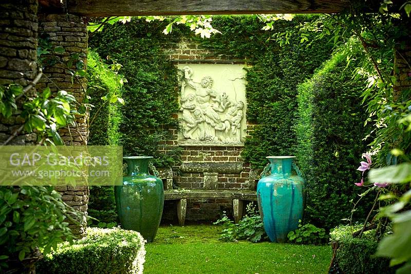 Klassische Steinsitze, umgeben von dekorativen Urnen und klassischer Skulptur. Die Rosenpergola, Highgrove, Juni 2019