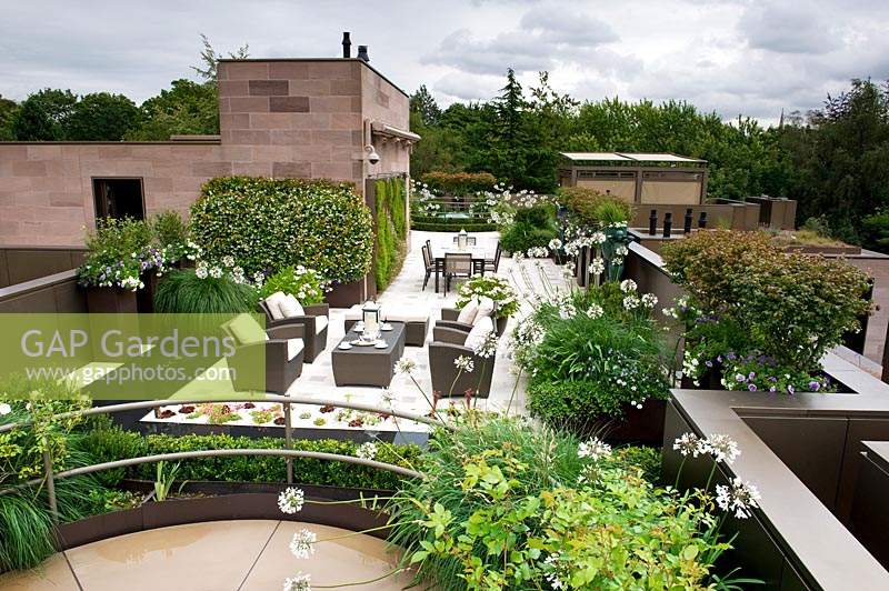 Blick über den modernen städtischen Dachgarten mit Anordnung der verschiedenen Sitzbereiche und Pflanzen an Wänden, Hochbeeten und Töpfen