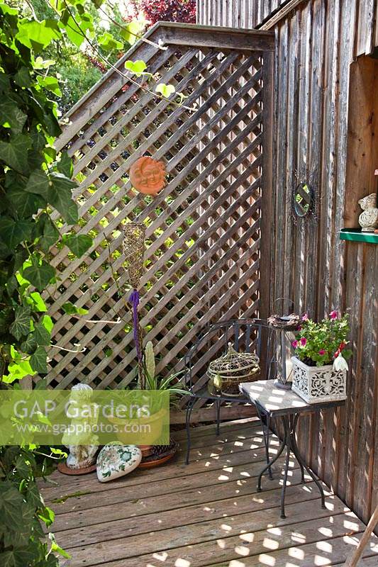 Das Gitter, das an einem Zaun und einem kleinen Holzdeck befestigt ist, bietet in einer Ecke eine Sammlung von Ornamenten und Topfpflanzen