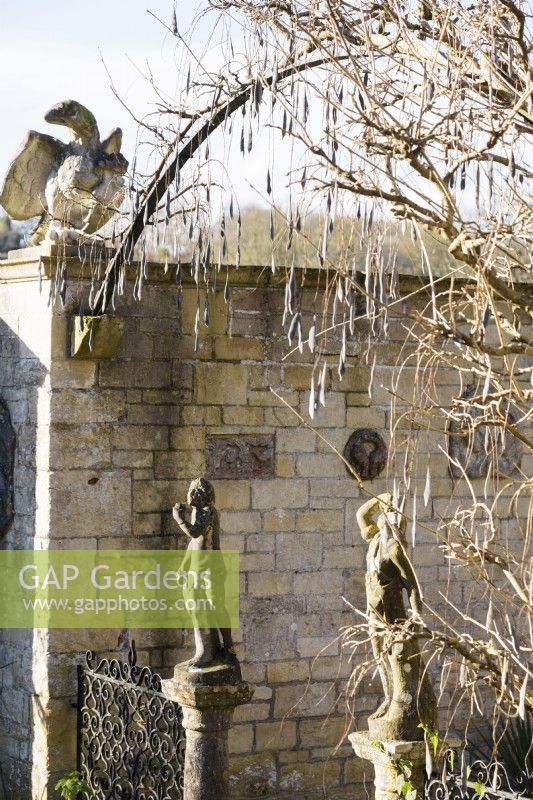 Metallbogen über einem gepflasterten Hof im Iford Manor im Januar, geschmückt mit seidigen Samenkapseln von Glyzinien 