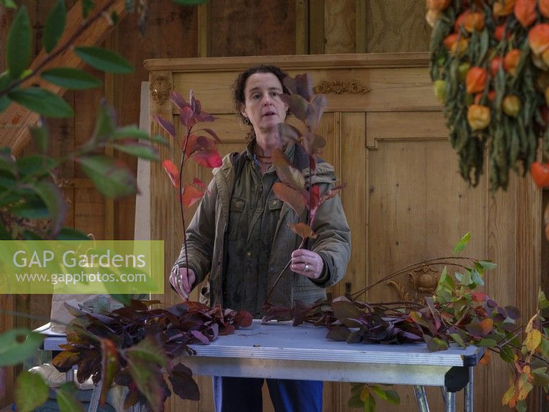 Scheunen-Inneneinrichtungswerkstatt. Die auf Laubfloristik spezialisierte Zanna Hoskins arbeitet mit Herbstfrüchten und Blättern aus ihrem Garten, um sie in saisonalen Arrangements zu verwenden. November, Herbst, Dorset, Großbritannien. 