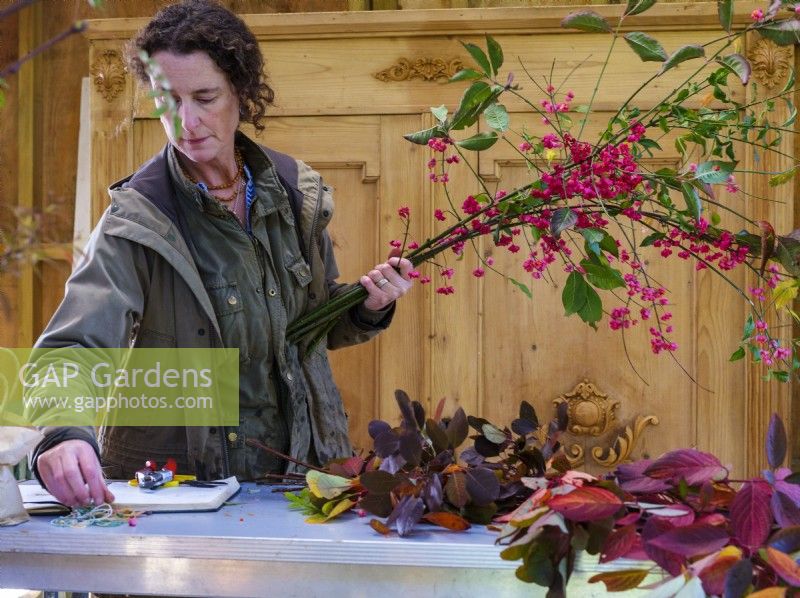 Werkstatt in einer Scheune, in der die auf Laub spezialisierte Floristin Zanna Hoskins mit Herbstfrüchten und Blättern aus ihrem Garten arbeitet, um sie in saisonalen Arrangements zu verwenden. November, Herbst, Dorset, Großbritannien. 