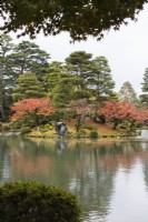 Blick über den Kasumigaike-Teich auf die Insel Horaijima. Bäume mit Herbstfärbung. 