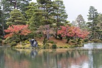 Blick über den Kasumigaike-Teich auf die Insel Horaijima. Bäume mit Herbstfärbung. 