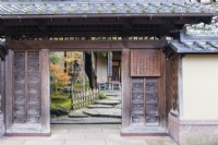 Blick in den Eingang zum Haus und Garten mit Hinweisen auf Japanisch und breiten Trittsteinen im Eingang und einem niedrigen Bambusgeländer. 